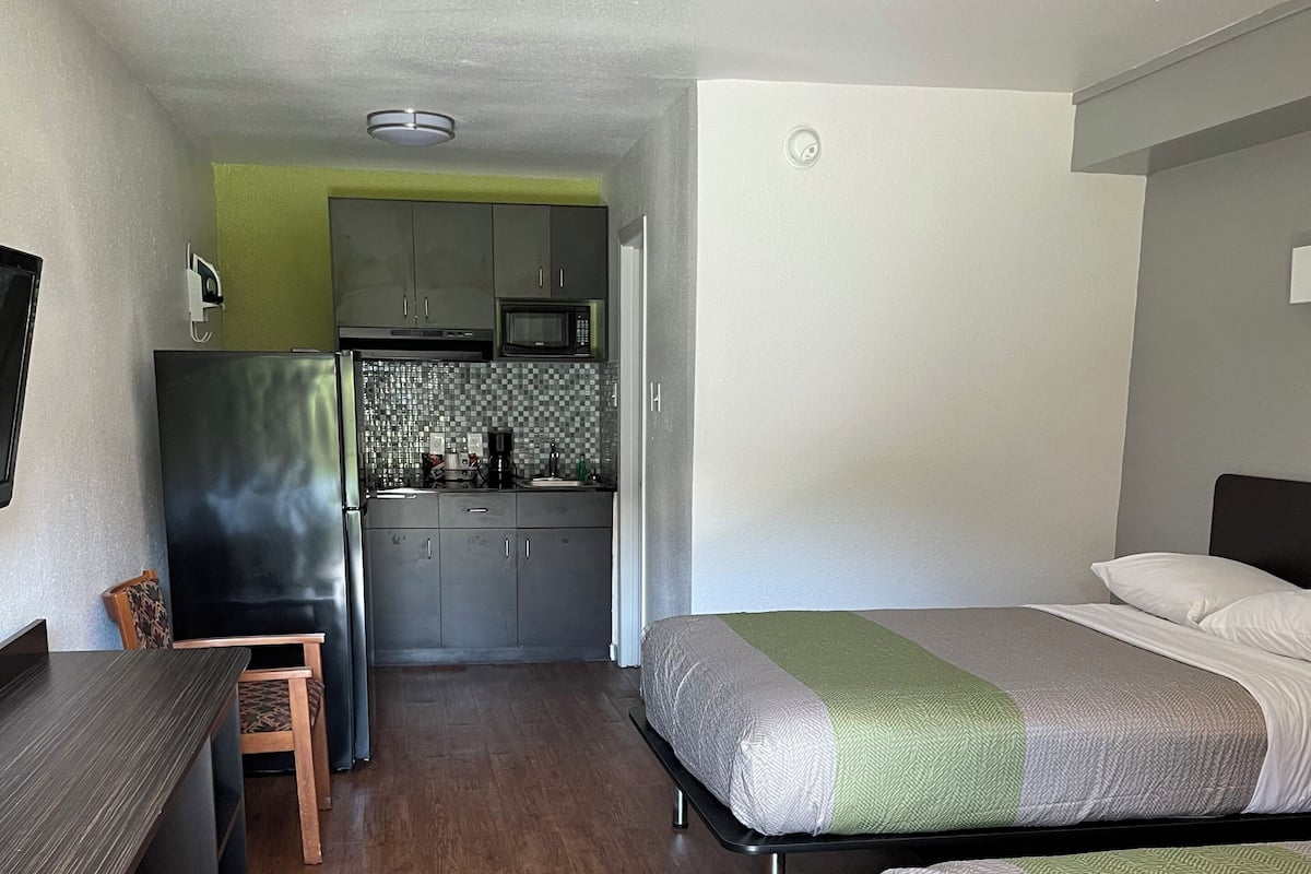 A compact room with a bed, a desk, a chair, a kitchenette, and a television.