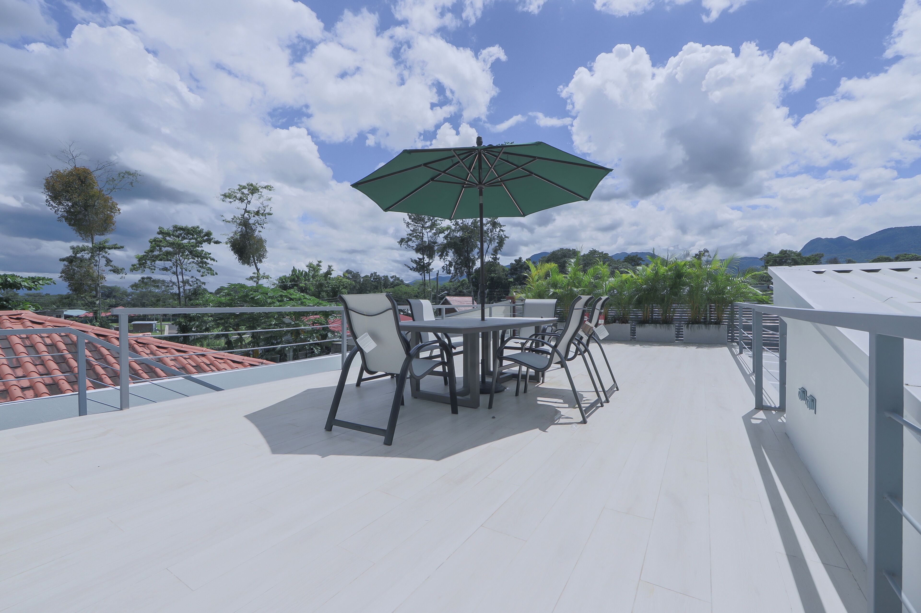 A rooftop terrace with a table and chairs, a green umbrella, and a view of the surrounding landscape.