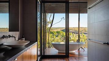 A modern bathroom with a large bathtub, a sink, and a view of a forested landscape.