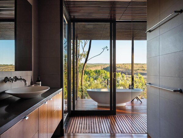 A modern bathroom with a large bathtub, a sink, and a view of a forested landscape. - El Questro - Homestead (Durack)