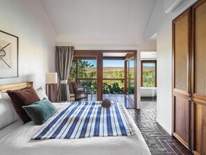Una habitació d'hotel amb un llit, vista a l'exterior i una porta de fusta.