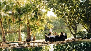 A dining area with a table set for six, surrounded by palm trees and a body of water. - El Questro - Homestead (Durack)