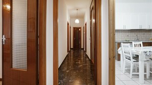 Ein Flur mit Holztüren und Marmorboden, der zu einem Küchenbereich mit weißen Schränken und einem Esstisch führt.