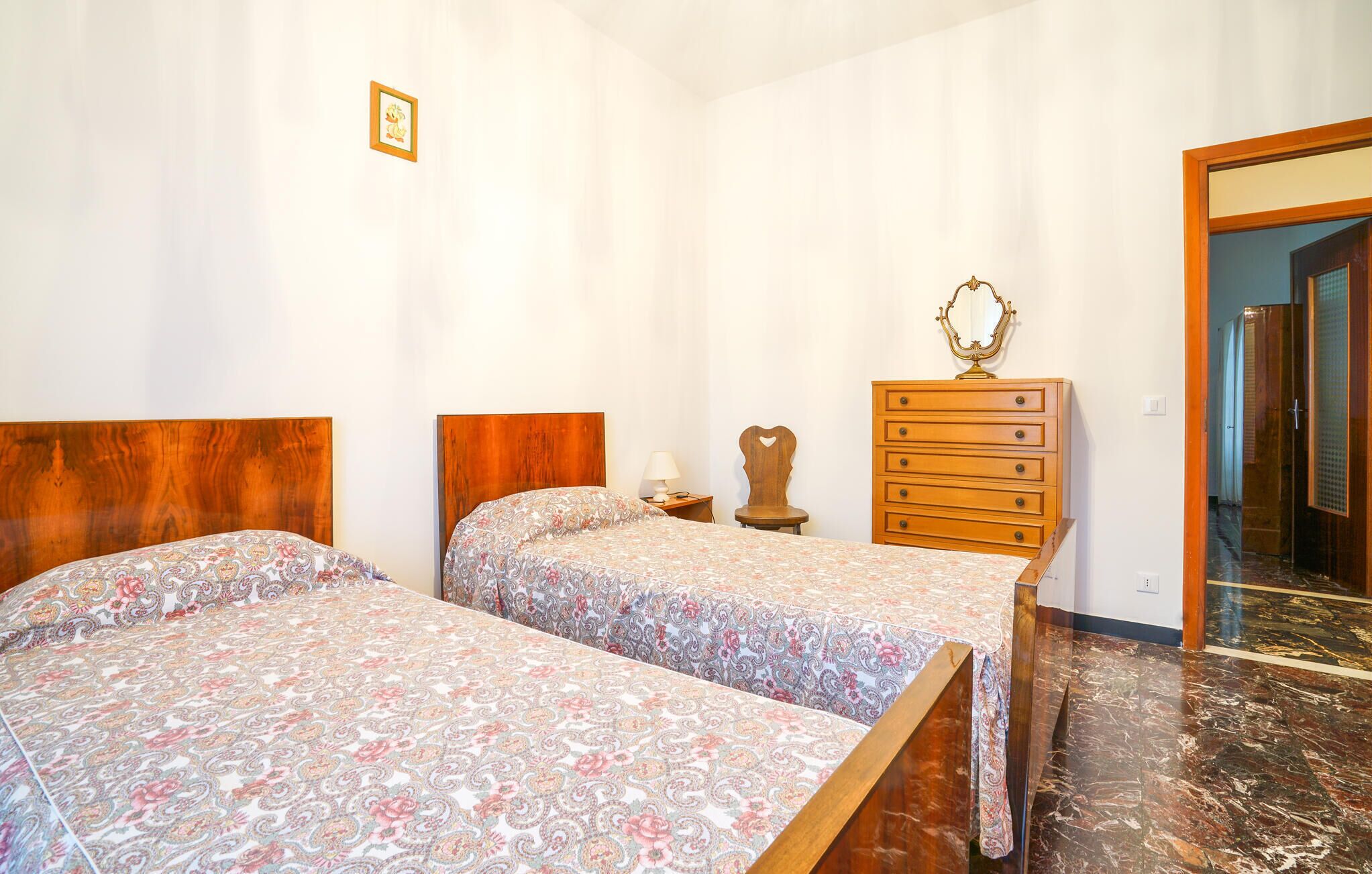 A bedroom with two beds, a wooden dresser, a mirror, and a door leading to another room.