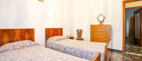 A bedroom with two beds, a wooden dresser, a mirror, and a door leading to another room.