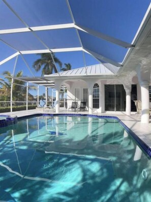 Une piscine à l’eau d’un bleu cristallin, entourée d’un bâtiment blanc orné de colonnes et dotée d’un espace abrité.