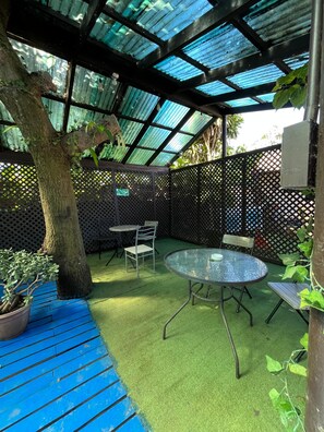 A covered outdoor area with a table and chairs, a potted plant, and a tree. - Hostal Vaianny (Hanga Roa)