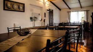 Un comedor con mesas y sillas de madera, una cesta trenzada negra sobre una mesa, y una obra de arte enmarcada en la pared.