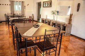 A dining area with multiple tables and chairs, a whiteboard on the wall, and a wooden floor. - Hostal Vaianny (Hanga Roa)