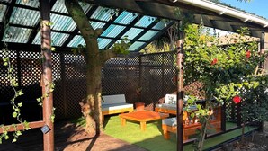 Un patio cubierto con mobiliario de madera, una mesita y un banco.
