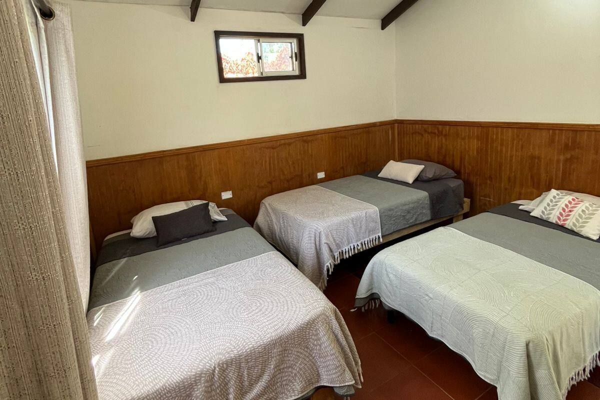 A dormitory room with four single beds, wooden headboards, a small window, and a tiled floor.