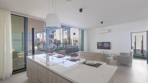A modern kitchen with a large island, dining area with chairs, a sofa, and a TV. - Villa Mae, Brand New, Stunning 4BDR Protaras Villa with Private Pool (Paralimni)