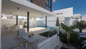 A modern outdoor living area with a pool, white furniture, and a well-maintained garden. - Villa Mae, Brand New, Stunning 4BDR Protaras Villa with Private Pool (Paralimni)