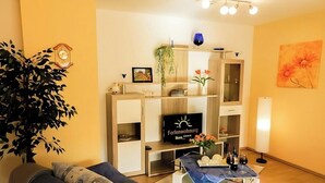 A living room with a TV, a plant, and a table with wine glasses. - Apartment Ilona – Modern & Cozy Stay Just 5 Minutes from the Fashion Outlet (Zweibrücken)