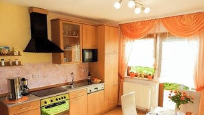 A kitchen with wooden cabinets, a stove, a sink, and a window with curtains. - Apartment Ilona – Modern & Cozy Stay Just 5 Minutes from the Fashion Outlet (Zweibrücken)