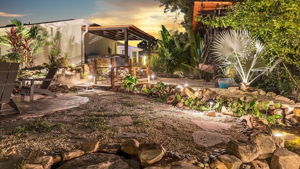 Un patio al aire libre bien iluminado con una pérgola de madera, asientos y una pequeña cascada.