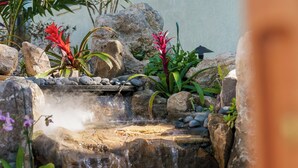 Una cascada pequeña en un jardín con rocas y plantas tropicales.