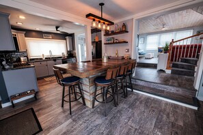 A modern kitchen with a central island, bar stools, and a dining area.