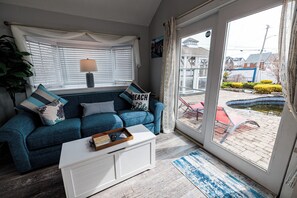 A living room with a blue sofa, white coffee table, and a view of the outside.