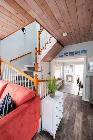 A spacious living area with a wooden staircase, a red sofa, and a white console table with drawers.