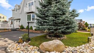 A two-story house with a well-maintained lawn, a large rock centerpiece, and a coniferous tree.