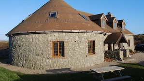 A stone house with a conical roof, a stone exterior, and two windows with wooden shutters. - The Roundhouse - Bliss by the sea (Lettermullen)