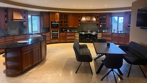 A modern kitchen with a curved island, built-in ovens, and a dining area with a table and chairs. - The Roundhouse - Bliss by the sea (Lettermullen)