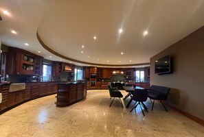 A spacious kitchen with a curved island, modern appliances, and a dining area with chairs. - The Roundhouse - Bliss by the sea (Lettermullen)