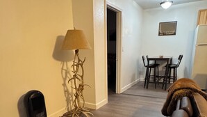A living room with a brown leather couch, a lamp, and a speaker. There is a dining area with a table and chairs in the background.