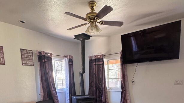 A living room with a sofa, a coffee table, a fireplace, a ceiling fan, and a TV mounted on the wall.