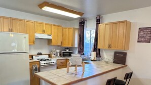 A modern kitchen with wooden cabinets, a central island, bar stools, and a stainless steel trash can.
