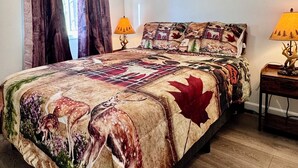 A bedroom with a large bed, a ceiling fan, wooden curtains, and three wall-mounted pictures.