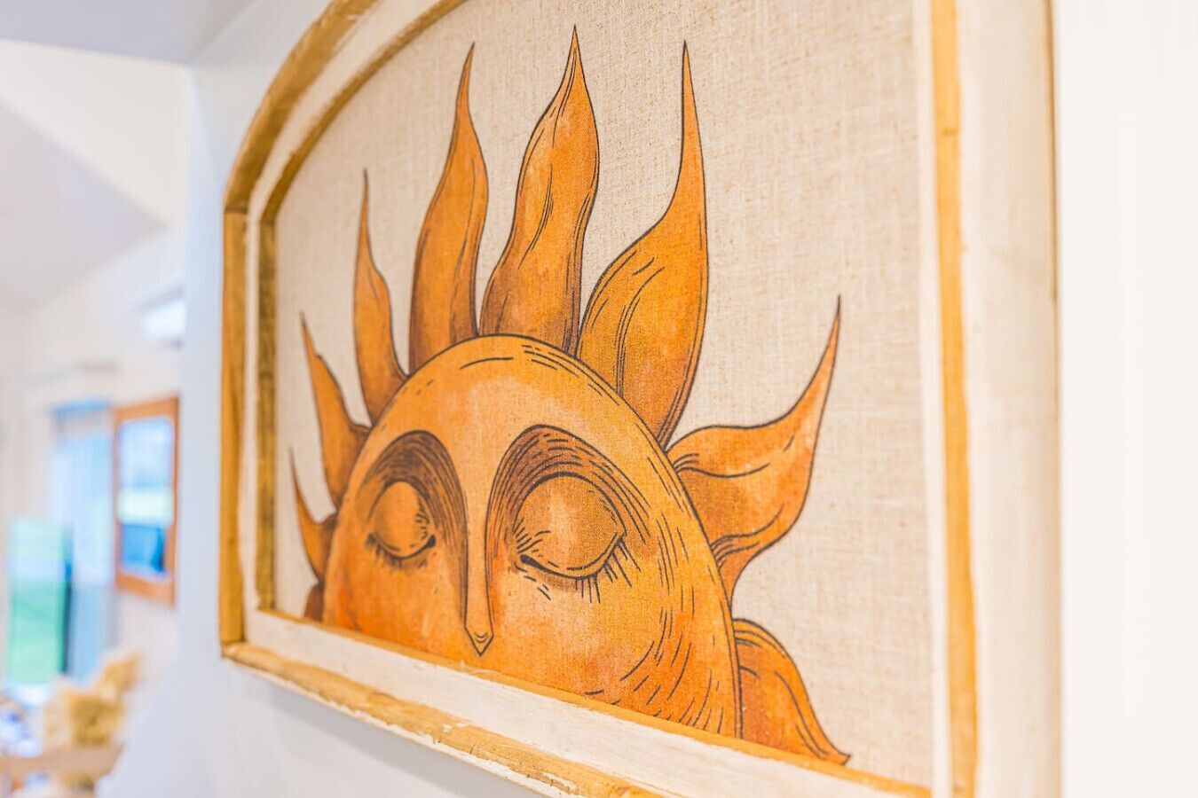Une œuvre d’art encadrée représentant un soleil stylisé avec un visage, peut-être une divinité solaire, accrochée à un mur.
