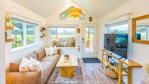 A cozy living room with a sofa, coffee table, and TV, large windows, and a wooden ceiling.