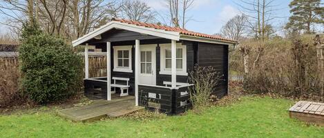Een kleine, gelijkvloerse blokhut met een veranda, ramen met witte kozijnen en een pannendak.