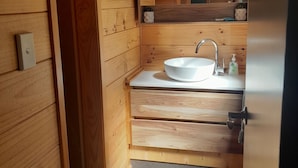 A wooden bathroom with a white sink, a mirror, and a shelf with toiletries.