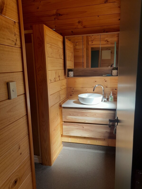 Et badeværelse i træ med en hvid vask, et spejl og en hylde med toiletartikler.