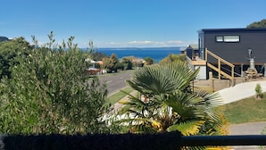 A modern building with a staircase leading to the entrance, surrounded by lush greenery and a view of the sea.