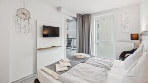 A modern bedroom with a bed, a mounted TV, a dreamcatcher, and a view of the outside balcony. - Fewo 3-13,Ostsee-Nordmole (Olpenitz)