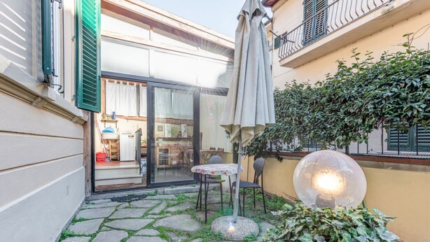 A courtyard with stone flooring, a table with chairs, a large glass door leading inside, and a spherical light fixture. - Garden House - Sweet Dreams in Florence (Firenze)