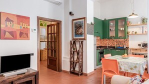 A living room with a TV, a sofa, a dining table with chairs, a kitchen with green cabinets, and artwork on the walls. - Garden House - Sweet Dreams in Florence (Firenze)
