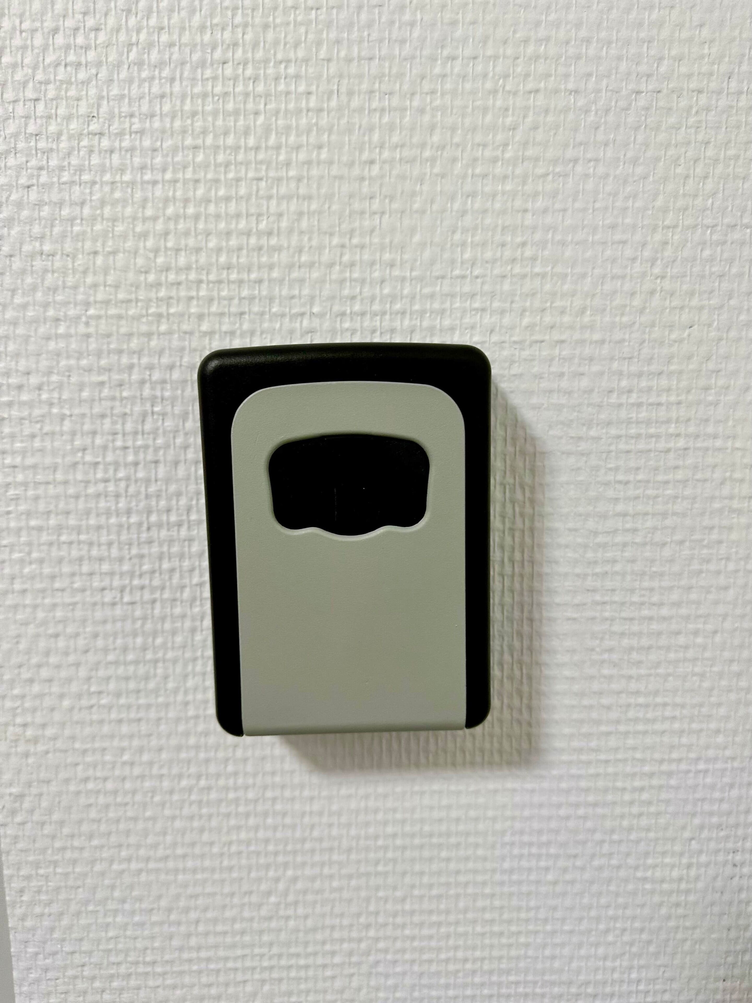 En hvid, struktureret væg med en intercom eller knap i sort og grå.
