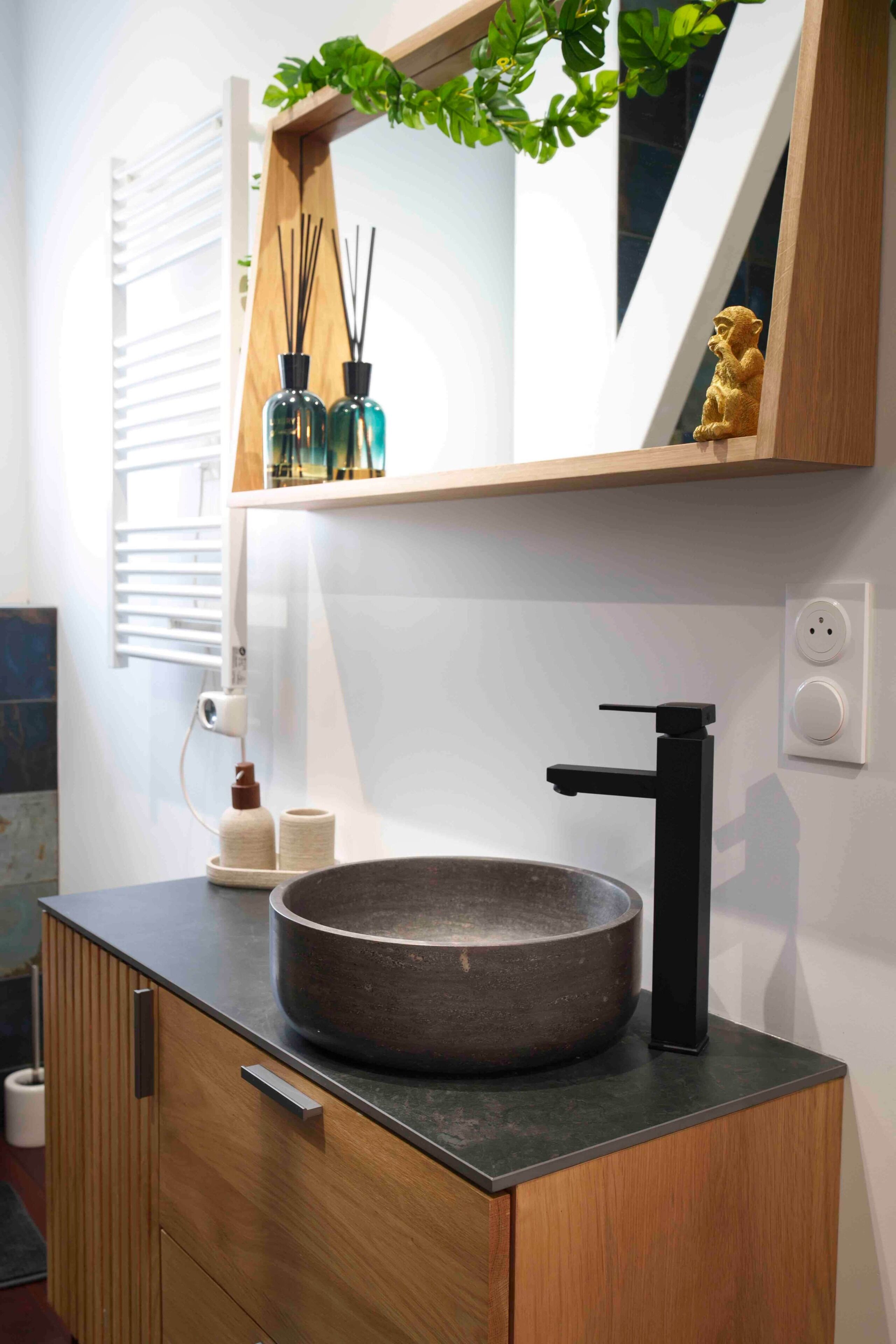Ein Badezimmer mit einem runden Waschbecken, einem schwarzen Wasserhahn, einem Holzschrank, einem Spiegel und einer kleinen Statue.