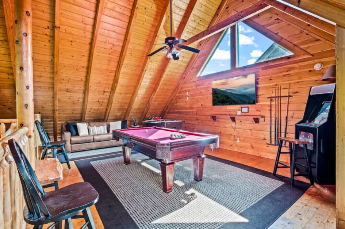 A cozy room with a pool table, a sofa, and a ceiling fan.