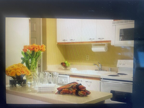 Una cocina con pileta, cocina y alacenas. Hay un florero con flores en la encimera.