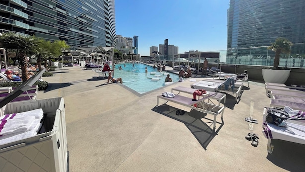 Un área de piscina en la azotea con sillas de descanso y sombrillas, rodeada de edificios modernos.