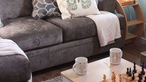 Een gezellige woonkamer met een grijze bank, gestreepte kussens, een schaakbord en een lamp op een bijzettafeltje.