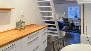 Une cuisine compacte dotée d’un plan de travail en bois, de meubles blancs et d’une échelle menant à une chambre à coucher située en mezzanine.