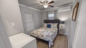 Une chambre à coucher comprenant un lit, un ventilateur de plafond, une table de chevet avec une lampe et une fenêtre avec des stores.