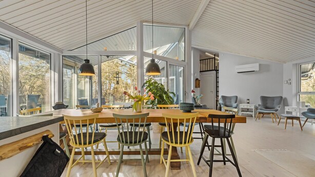 A spacious dining area with a large wooden table and multiple chairs, large windows offering views of trees, and pendant lighting. - 5 bedroom nice home in Fårevejle (Fårevejle)